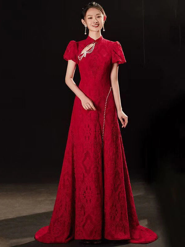 A woman modeling a floor-length red Open Back Lace Cheongsam/Qipao Dress With Train  gown with short puff sleeves, a high neckline, and a decorative embroidered chest detail, photographed against a dark studio background.