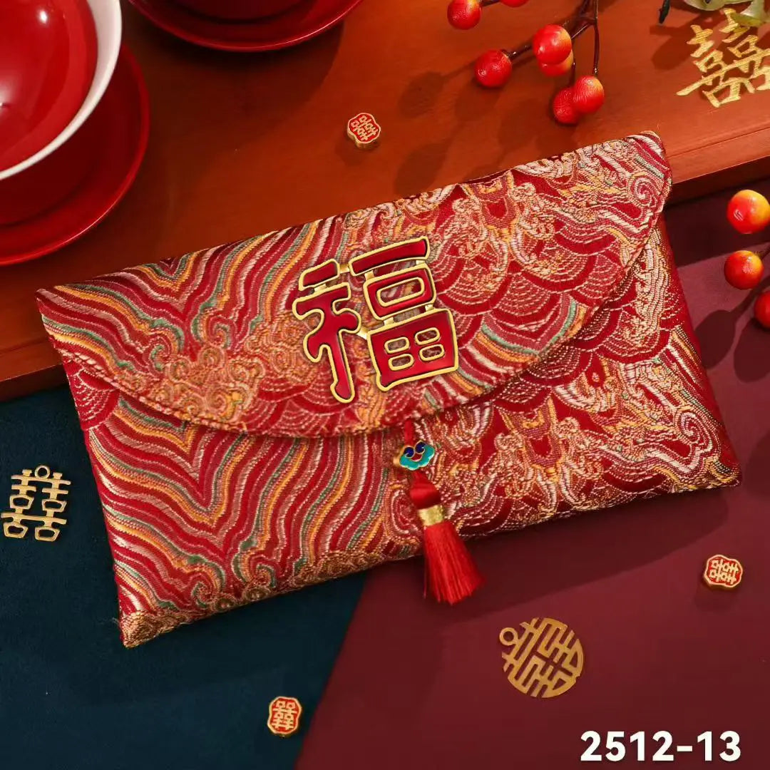 A red and gold embroidered Chinese envelope-style clutch with a large gold Chinese character on the front flap, decorative tassel, and multicolored wave patterns, shown on a styled tabletop with red dishes and decorative motifs.