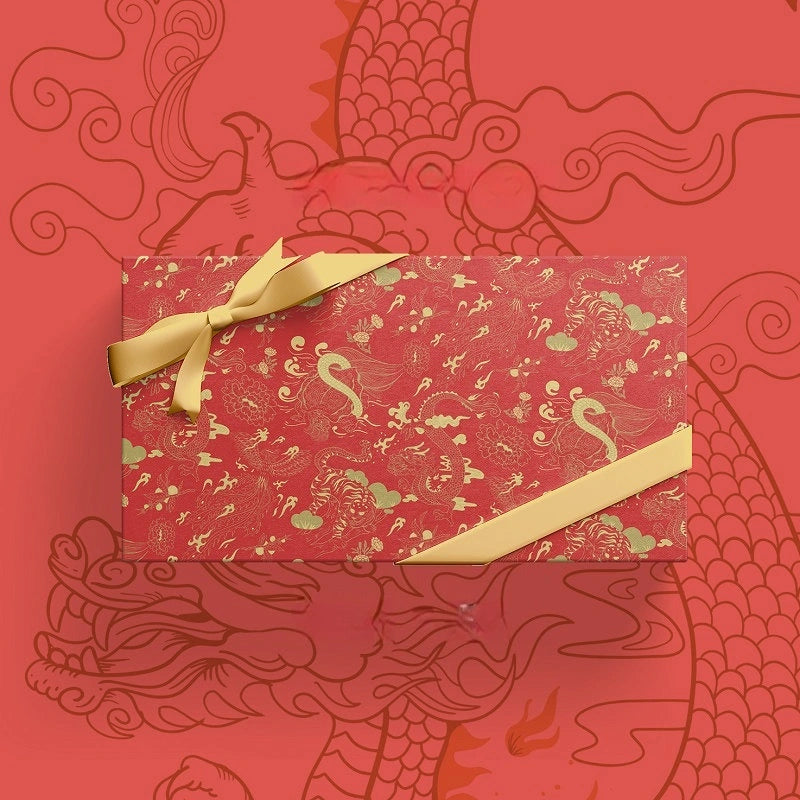 A rectangular gift box wrapped in red patterned paper with gold dragon and pheonix  motifs, tied with a gold ribbon bow and diagonal ribbon, set against a matching red patterned background.