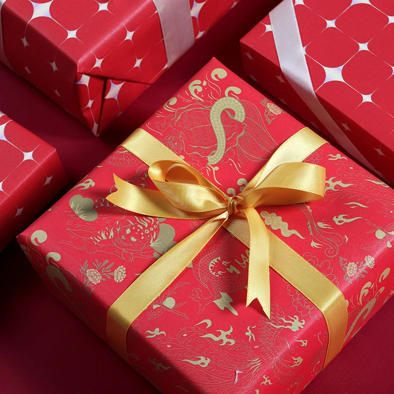 Red gift wrapping paper with gold dragon and phoenix patterns, tied with a shiny gold ribbon and bow, shown on a matching red background with other wrapped boxes.