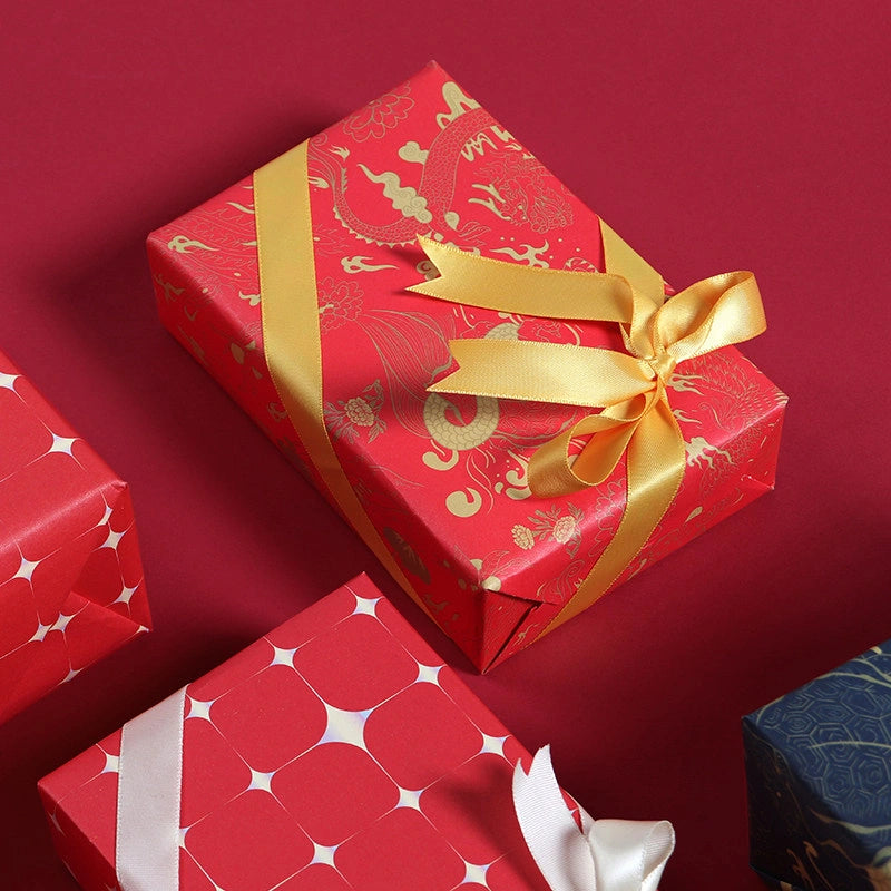 Red gift wrapping paper with gold dragon phoenix motifs and a gold ribbon bow, shown wrapped around a rectangular present on a dark red background.