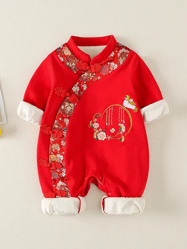 A baby's red Traditional Chinese Embroidered Baby Girl Qipao Romper romper with traditional Chinese styling, featuring floral embroidery, decorative buttons, and white cuffs and foot coverings, displayed against a light beige wall.