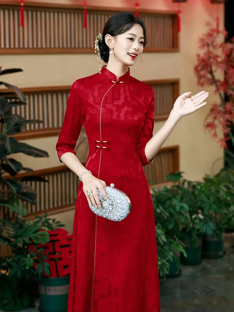 A woman wearing a red Chinese aline cheongsam/qipao dress with three-quarter sleeves and a silver beaded clutch, posing in front of a traditional wooden screen and potted plants 