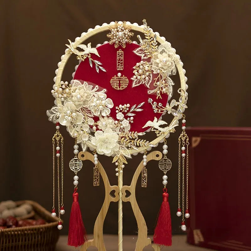 red Chinese Bridal Round Hand Fan with Tassels  on a stand against a dark background