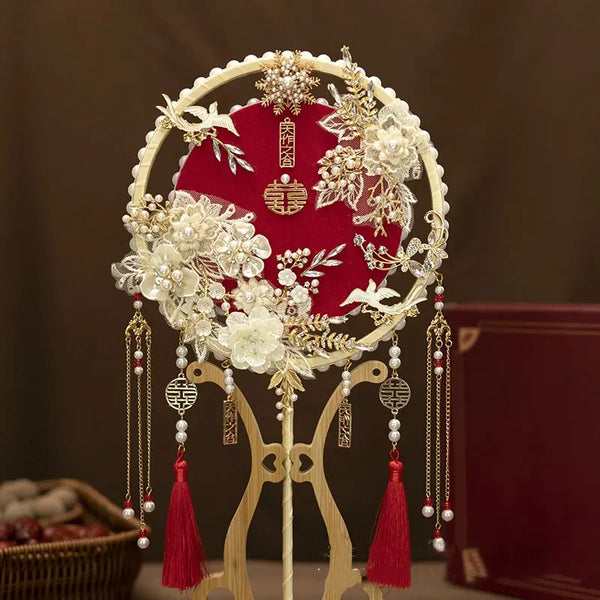 red Chinese Bridal Round Hand Fan with Tassels  on a stand against a dark background