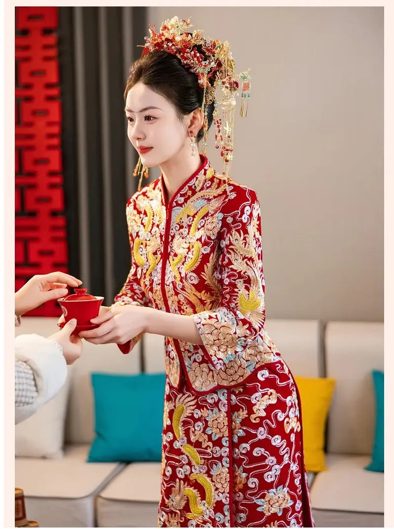 Woman in traditional chinese  red and gold dragon phoenix qun kaw dress with decorative hairpiece in a living room.
