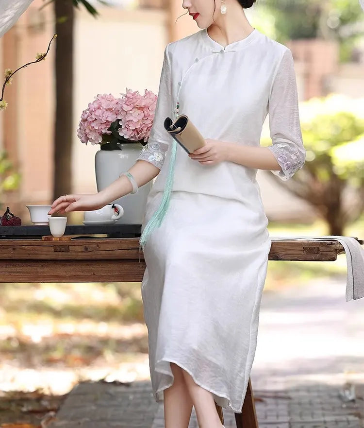 A chinese Woman in a white Loose A line Cheongsam Qipao Dress  holding a book outdoors with blurred background