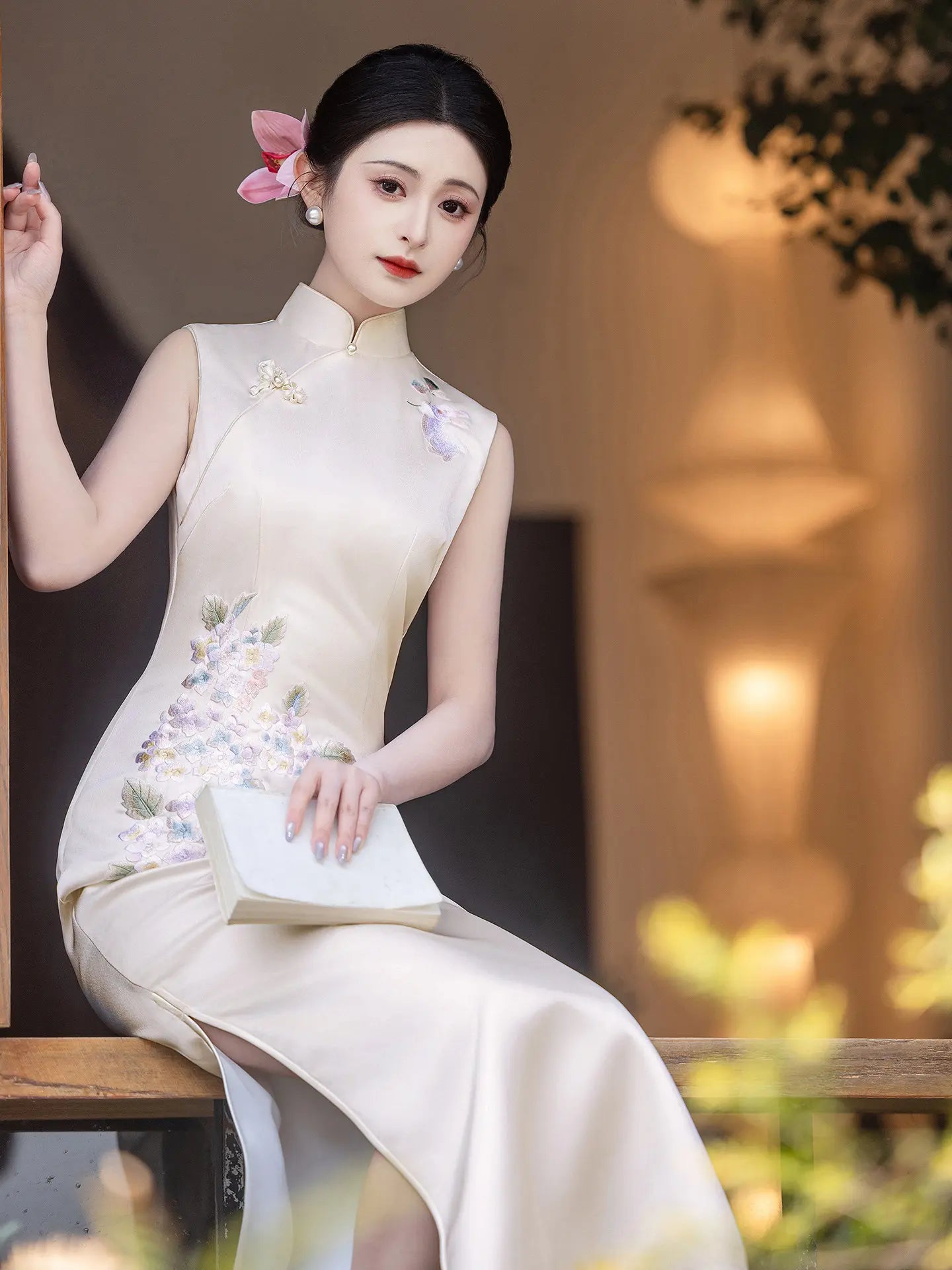 Woman in a traditional white Luxury Embroidered New Chinese Style Sleeveless Qipao Dress outfit with floral patterns sitting on a wooden bench.