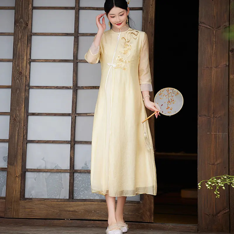 Woman in a light yellow Floral Embroidered Loose A line Cheongsam Qipao Dress holding a fan against a wooden panel background