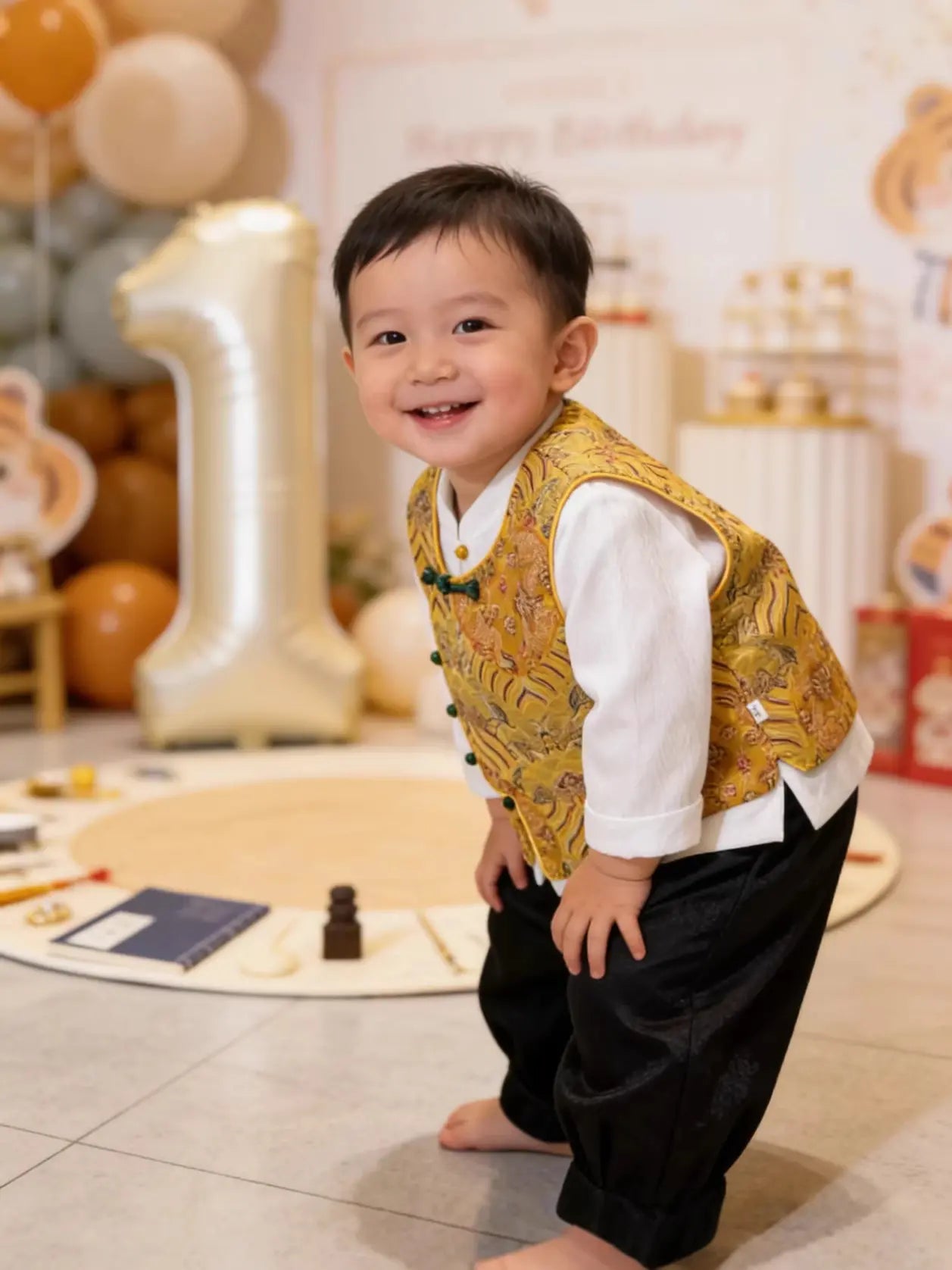 Child in a yellow New Chinese Style Baby Boy Traditional Tang Suit Dragon Vest Set outfit with balloons and a number one in the background